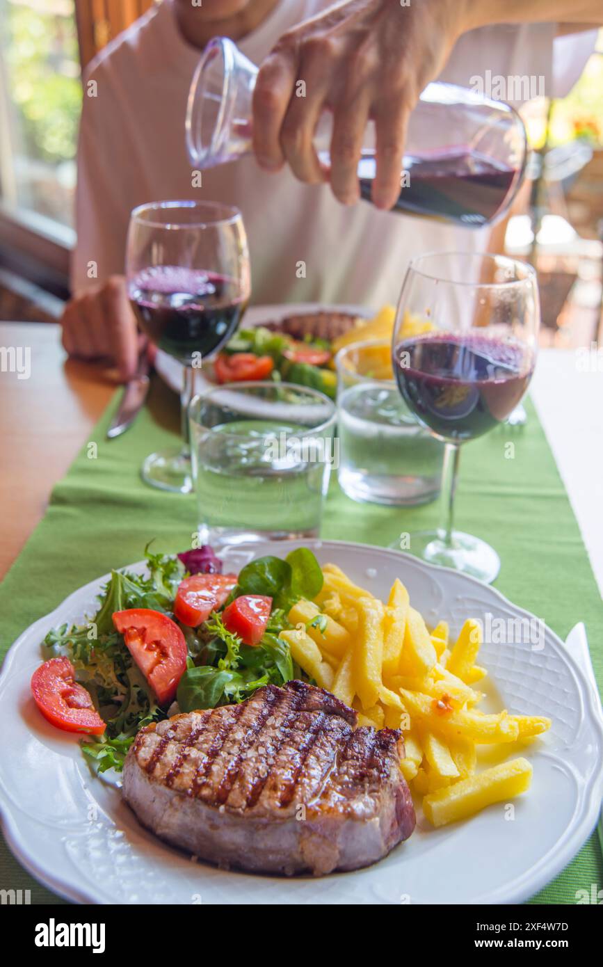 Sirloin steak with salad and chips, and man pouring red wine in a glass ...