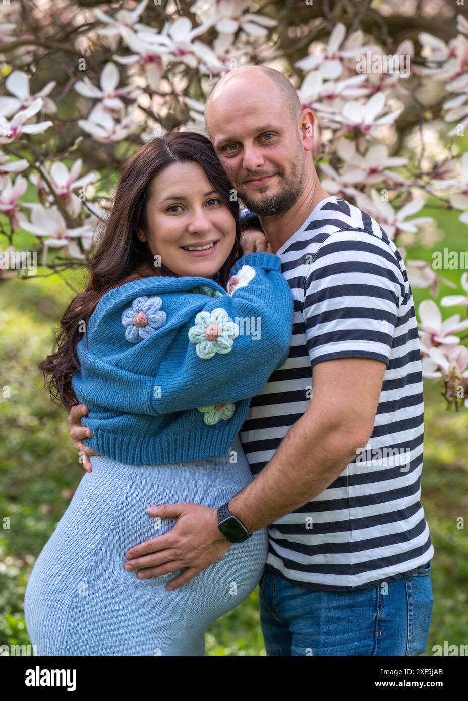 A man tenderly hugs his pregnant wife. The woman is wearing a blue ...