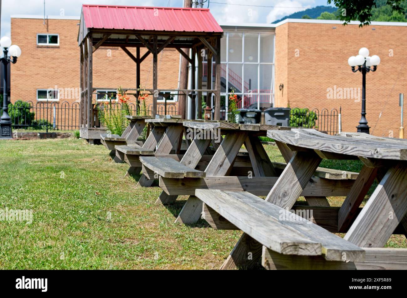 Four worn and warped picnic tables in a small park with a gazebo Stock Photo