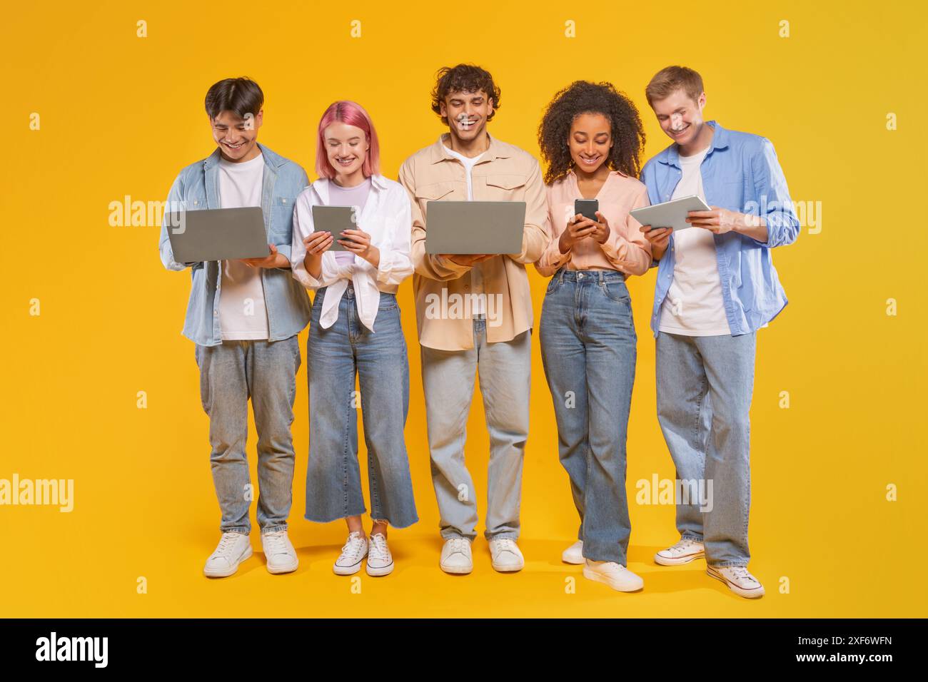 Five Diverse Young Adults Using Technology In Front Of Yellow Stock Photo