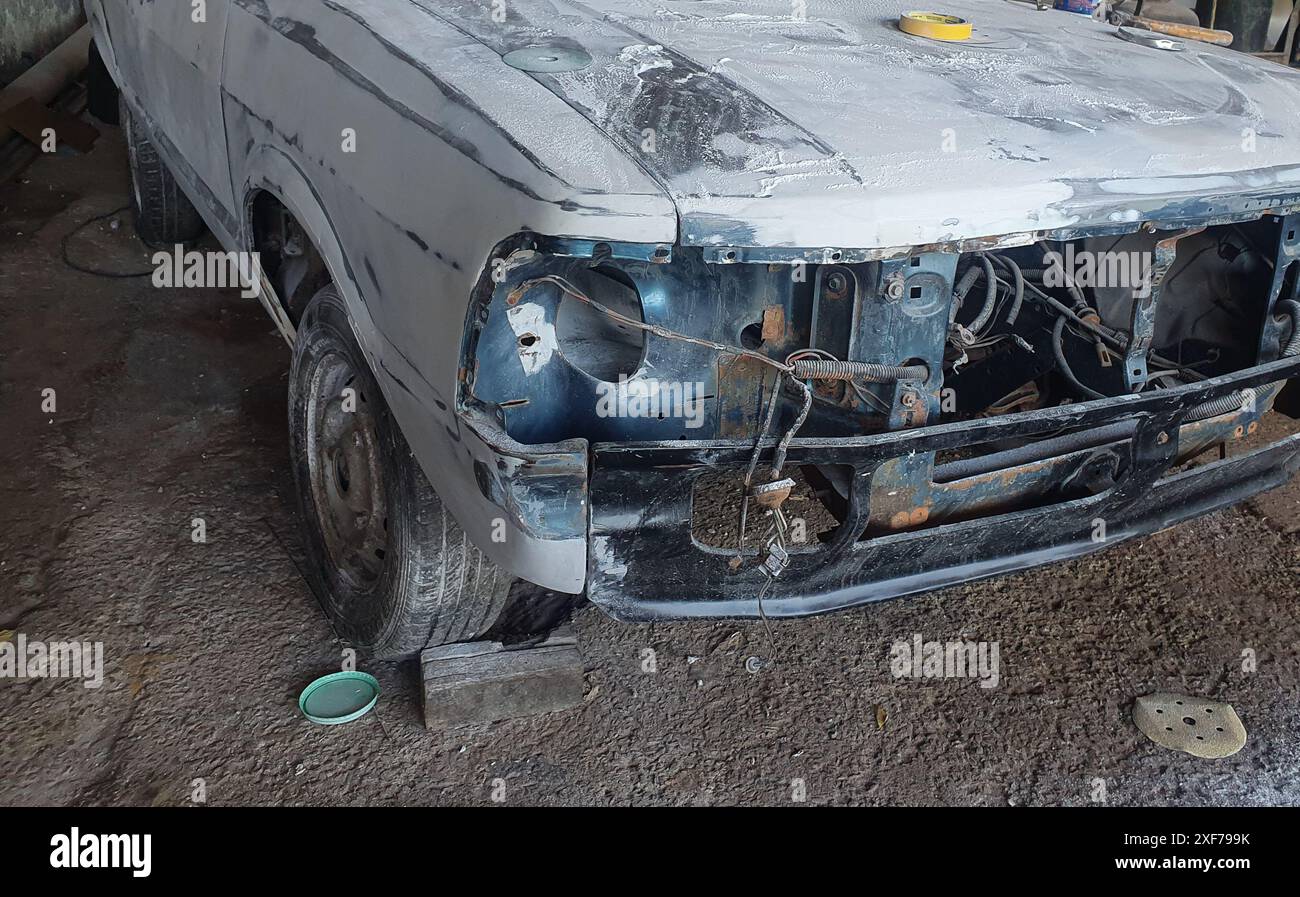 A car with old bodywork, dismantled bumper, all dusty, white powder, bald tire and a grinder on the cement floor. Stock Photo