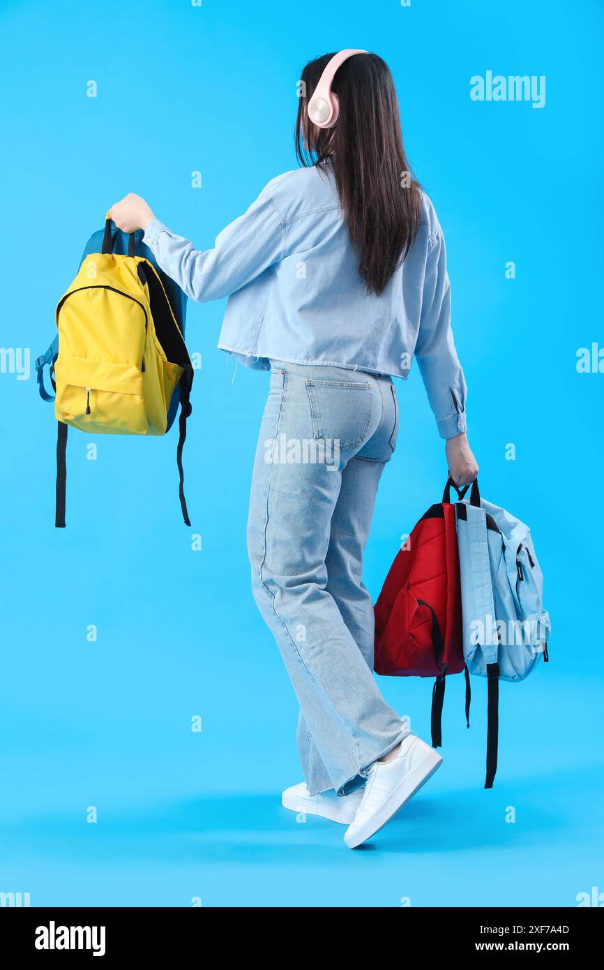 Female student in headphones with backpacks on blue background, back ...