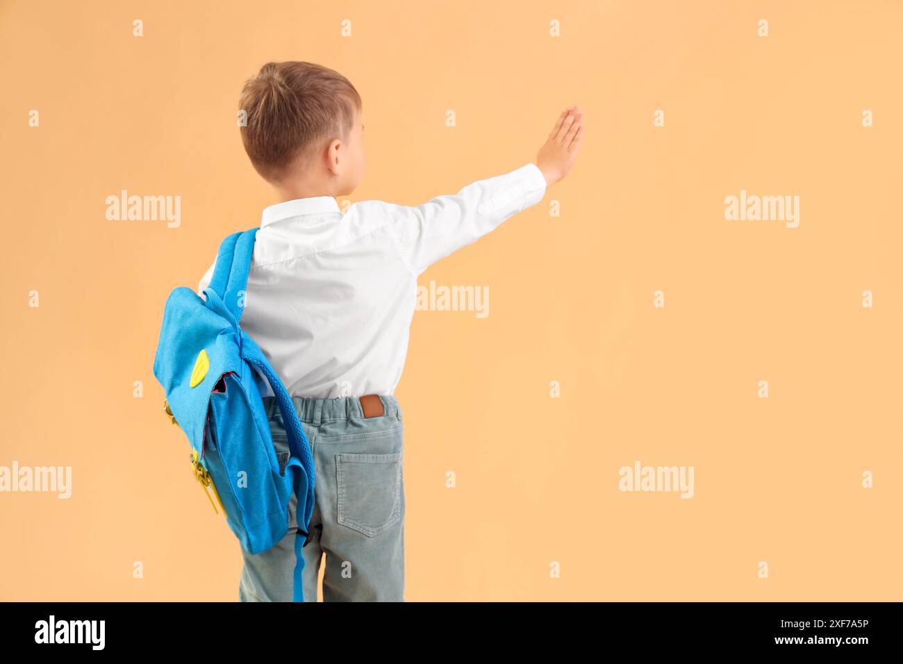 Little schoolboy with backpack waving hand on orange background, back ...