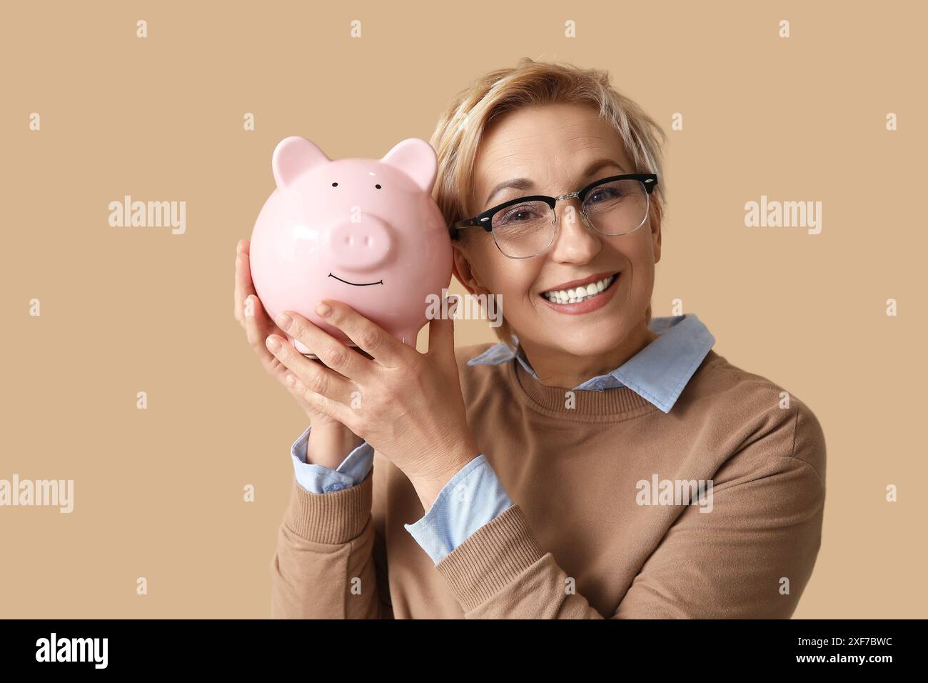 Happy mature woman with pink piggy bank on brown background Stock Photo ...