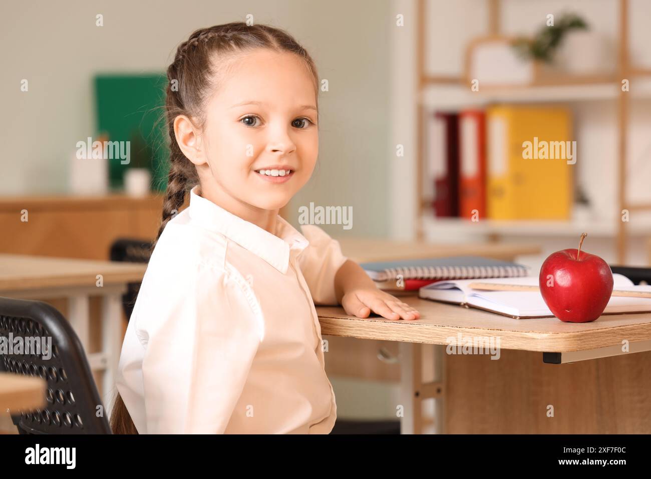 Little schoolgirl with apple at desk in classroom Stock Photo - Alamy