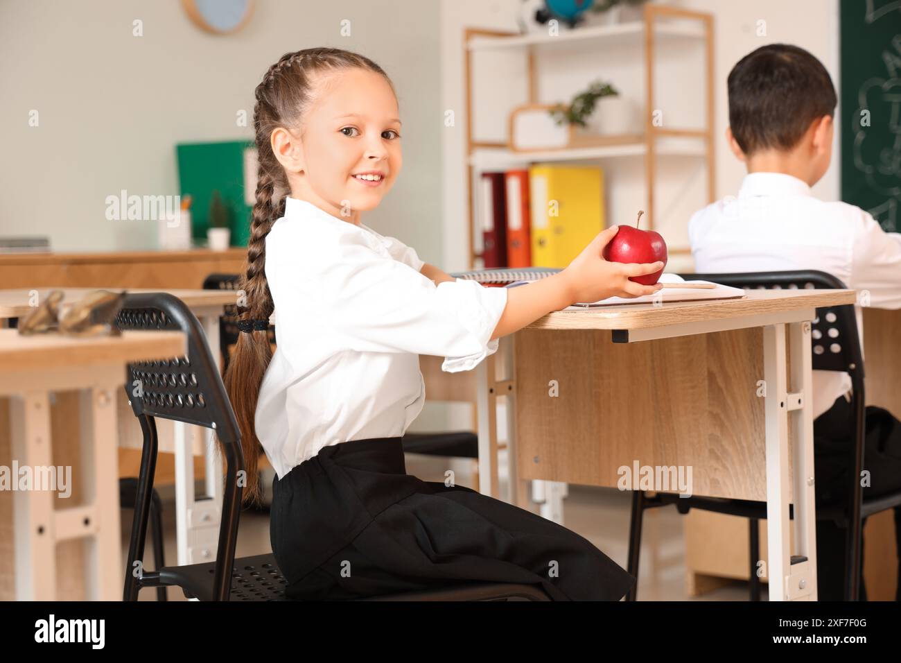 Little schoolgirl with apple at desk in classroom Stock Photo - Alamy