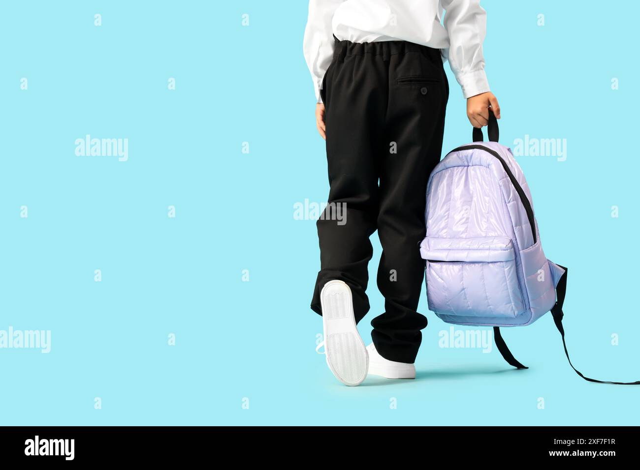 Little schoolboy with backpack walking on blue background, back view ...