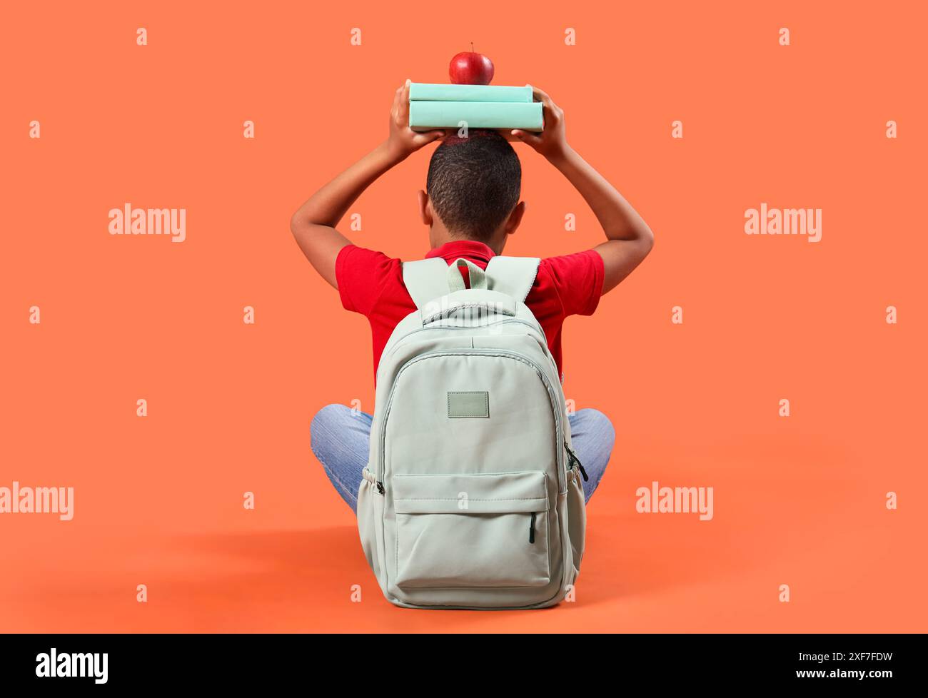 Little schoolboy with backpack holding books and apple on orange ...