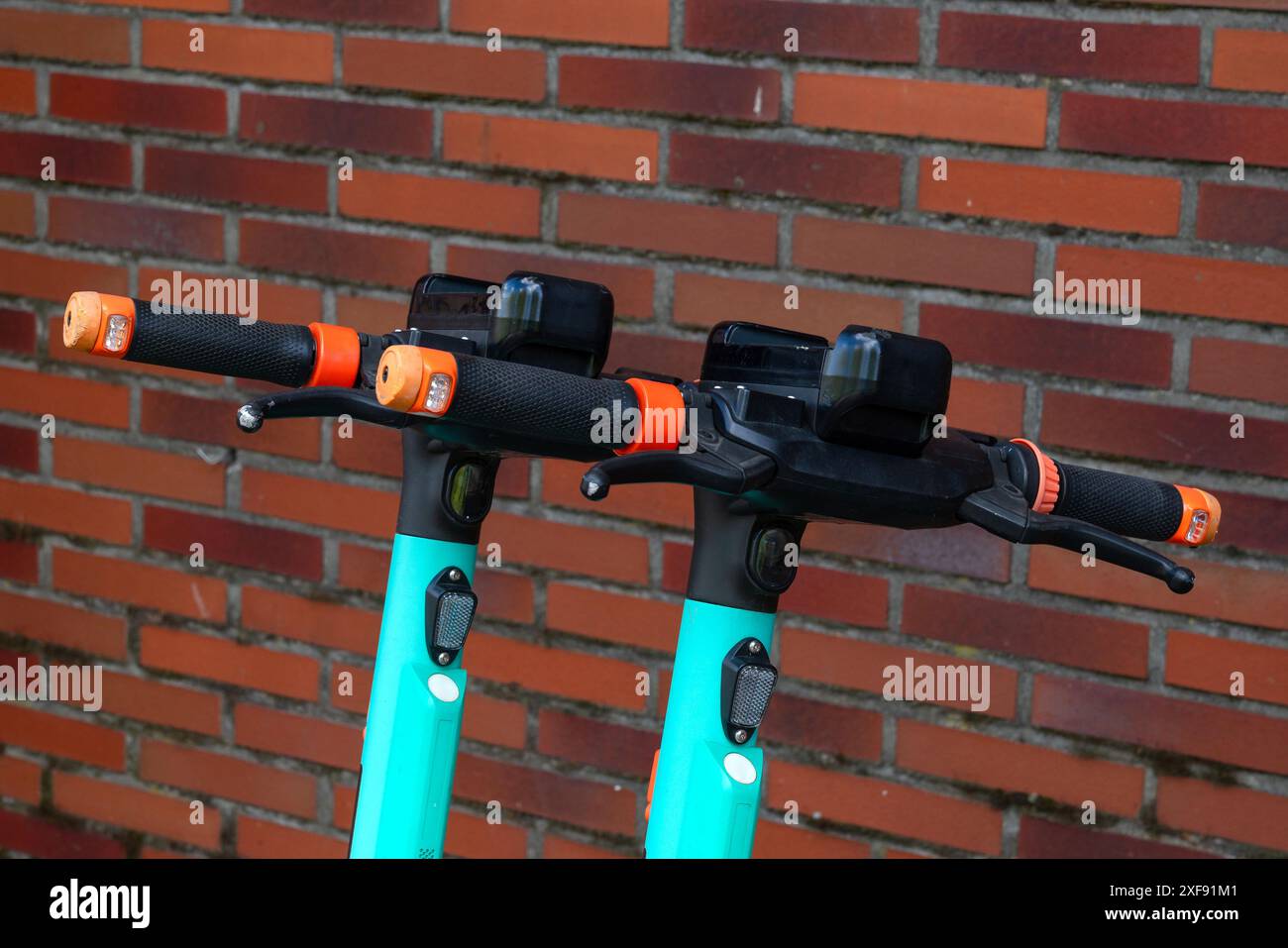 Two teal electric scooters are parked side-by-side against a brick wall.  Stock Photo