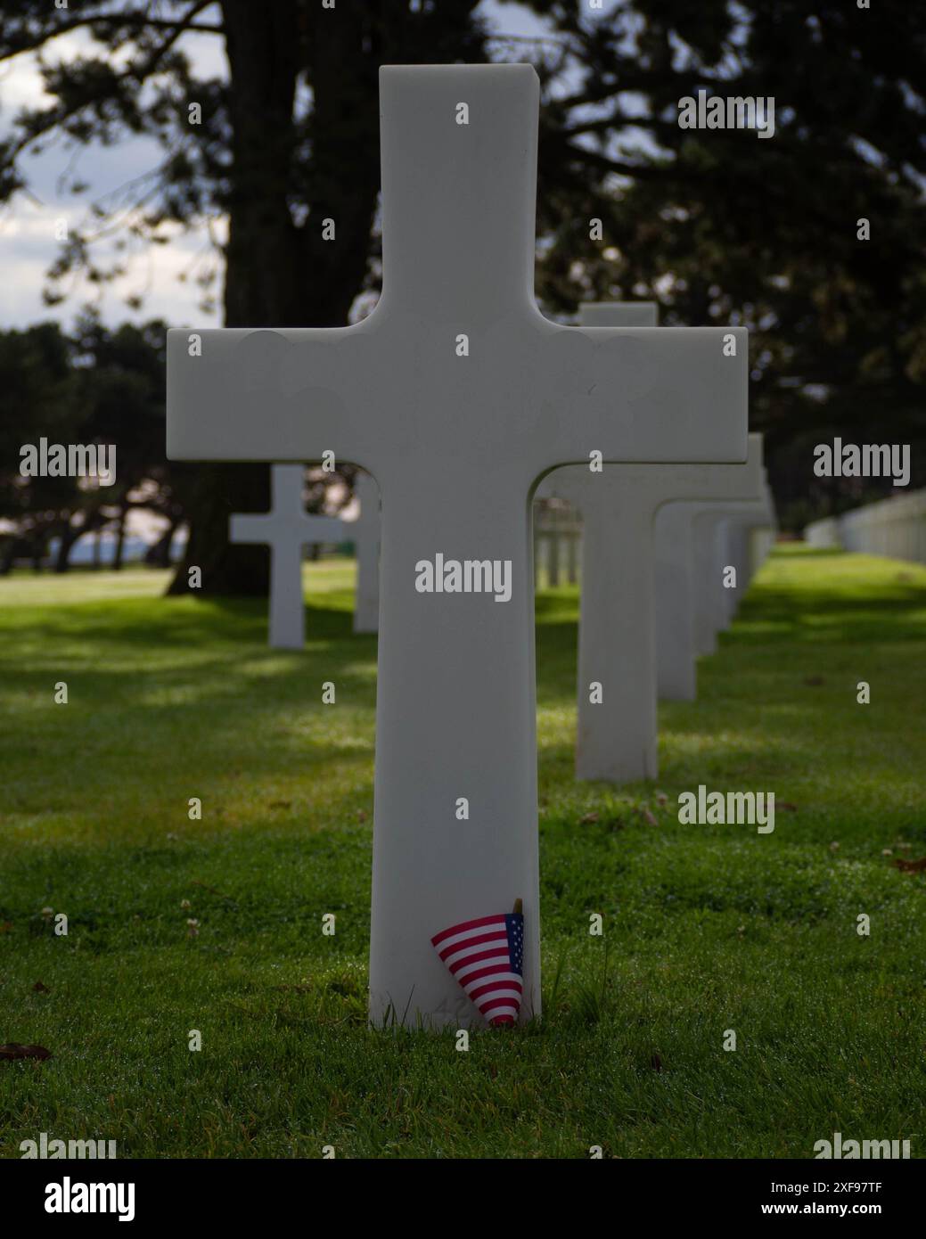 A row of white crosses in a military cemetery with an American flag on ...