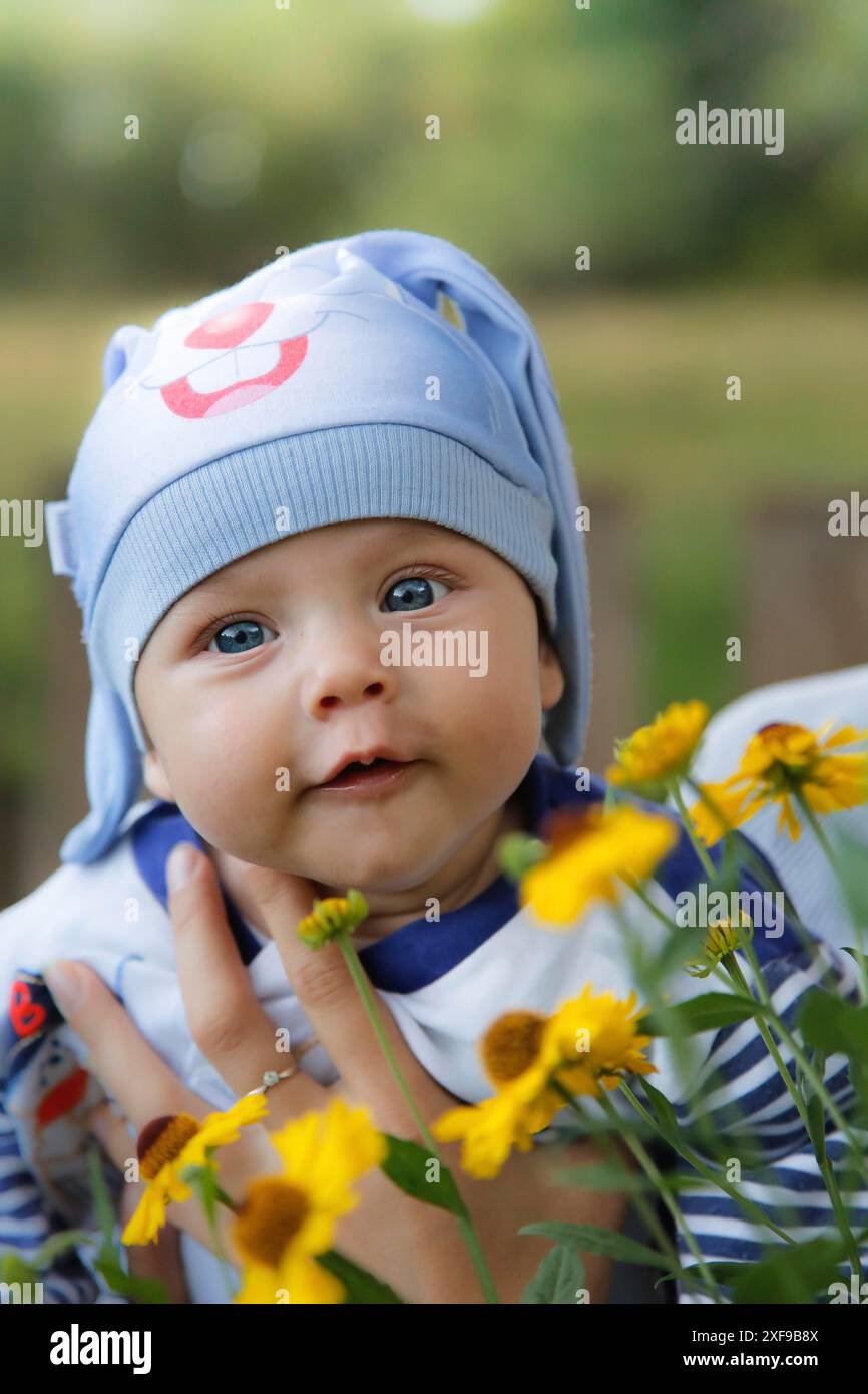 A cute baby wearing a blue hat is surrounded by yellow flowers in an ...
