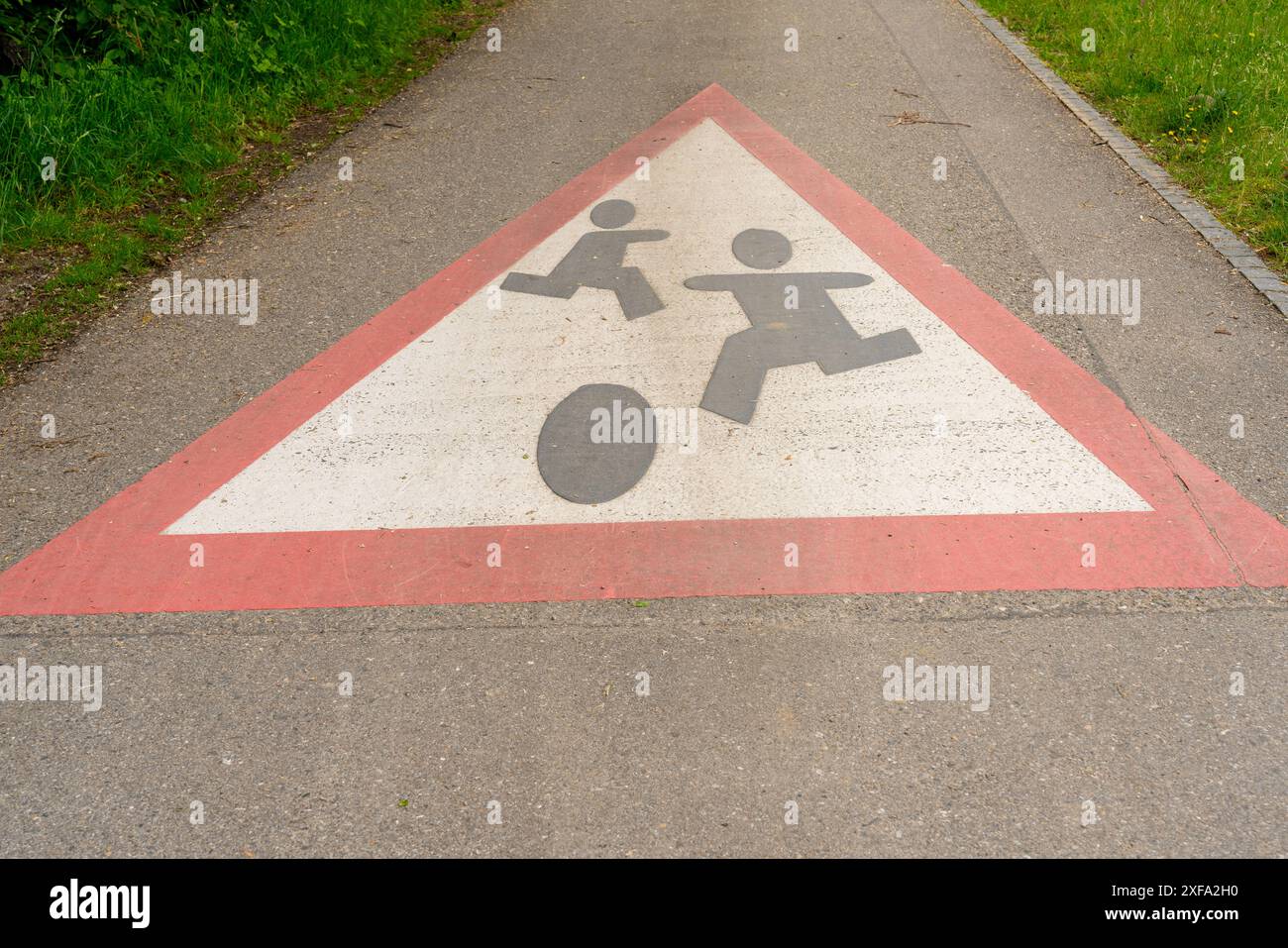 Big playing children warning sign painted on a small street, leading through meadows and brush. Stock Photo