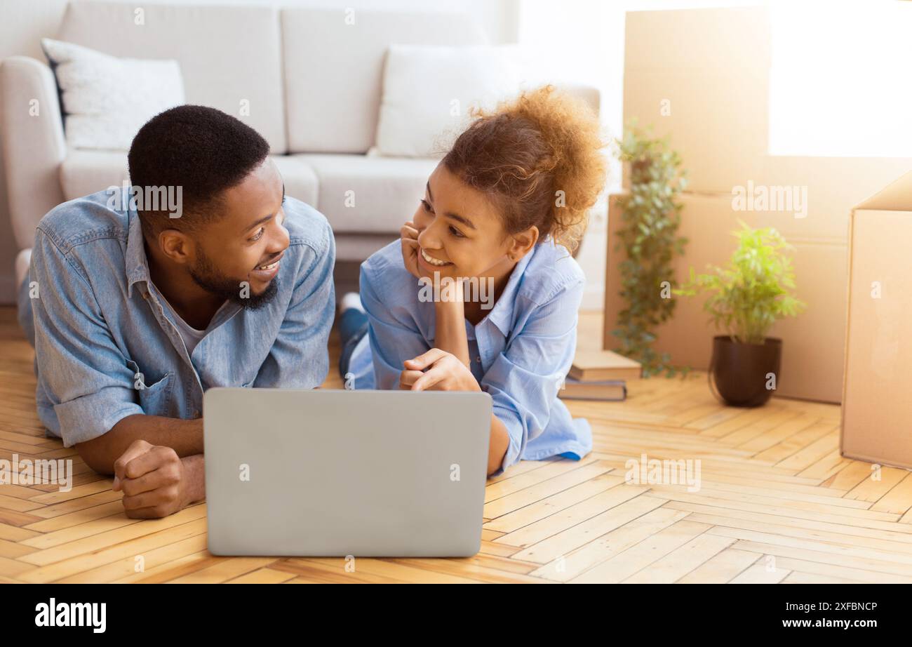Spouses Using Laptop Lying On Floor Among Moving Boxes Indoor Stock Photo