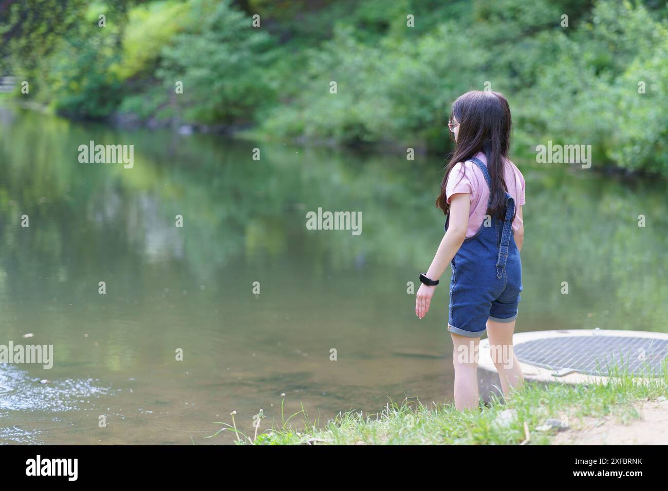 A little cute teenage girl stands with her back to the camera near a ...