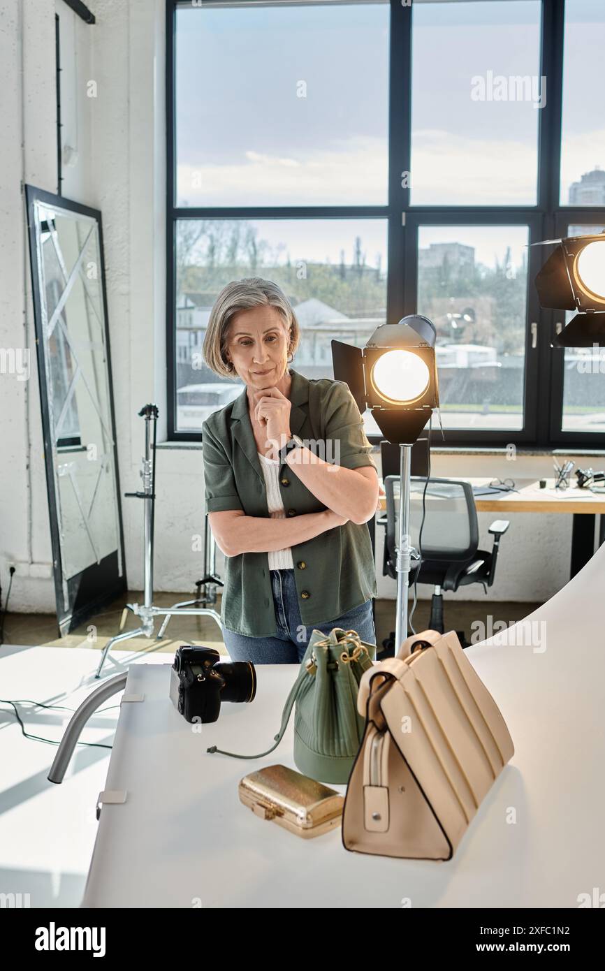 Middle-aged woman standing confidently and looking at bag in modern photo studio. Stock Photo