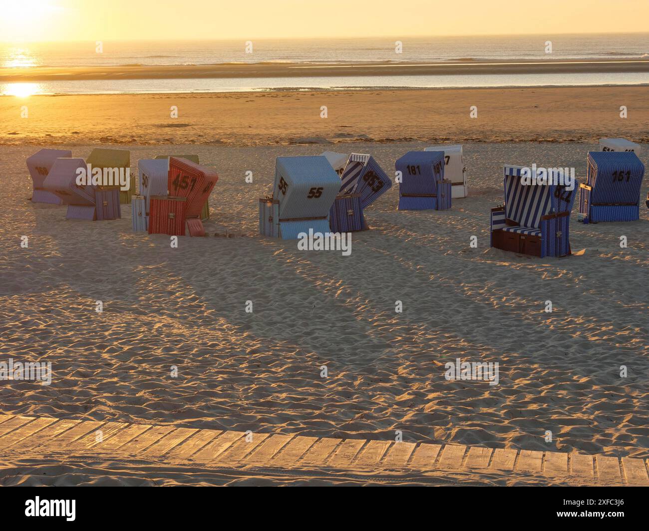 Colourful beach chairs cast long shadows in the sand at sunset ...