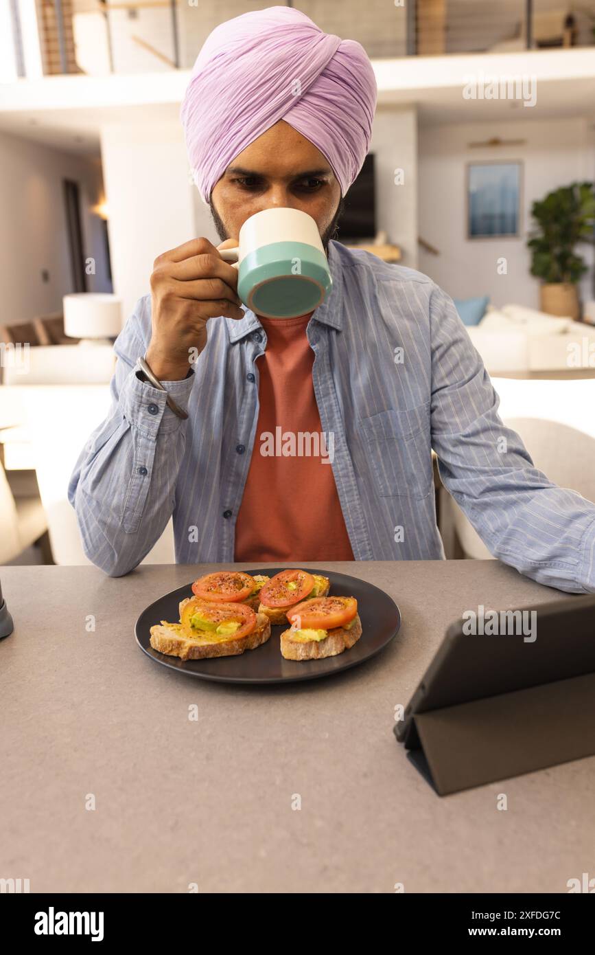 Drinking coffee and using tablet, man having breakfast with avocado toast Stock Photo