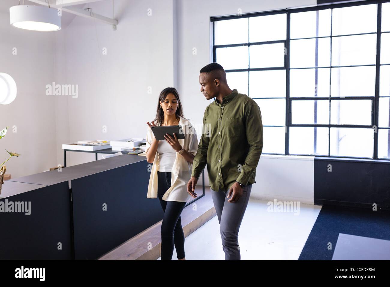 Discussing work, colleagues walking in modern office while using digital tablet Stock Photo