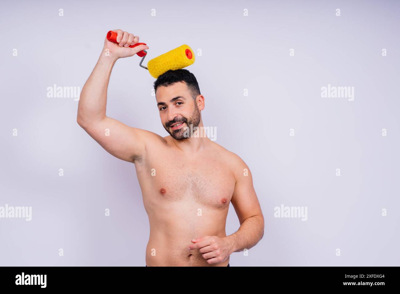 Young employee handyman using paint roller hold face isolated on background studio. Stock Photo
