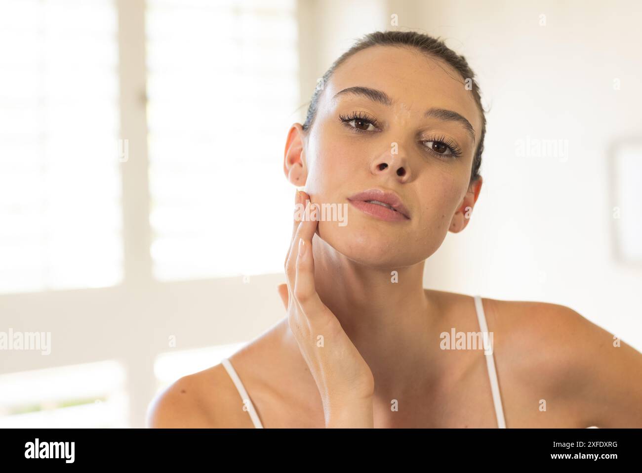 Touching her face, young woman with clear skin looking at camera Stock Photo