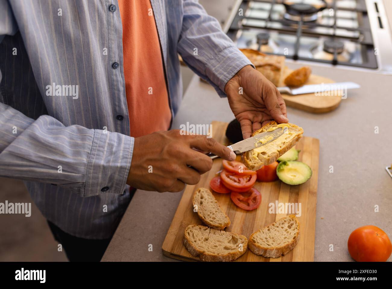 Spreading butter on bread, man preparing sandwich with fresh vegetables in kitchen Stock Photo