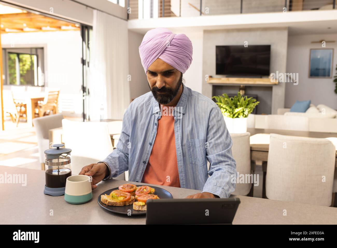 Working from home, man using tablet while having breakfast with coffee Stock Photo