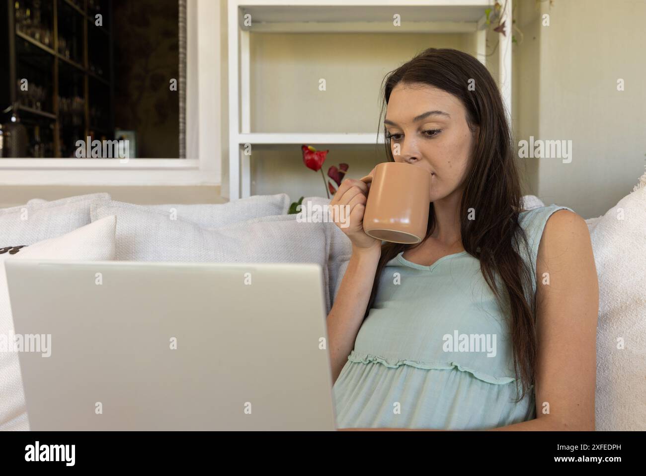Drinking coffee while using laptop, young woman working from home Stock Photo