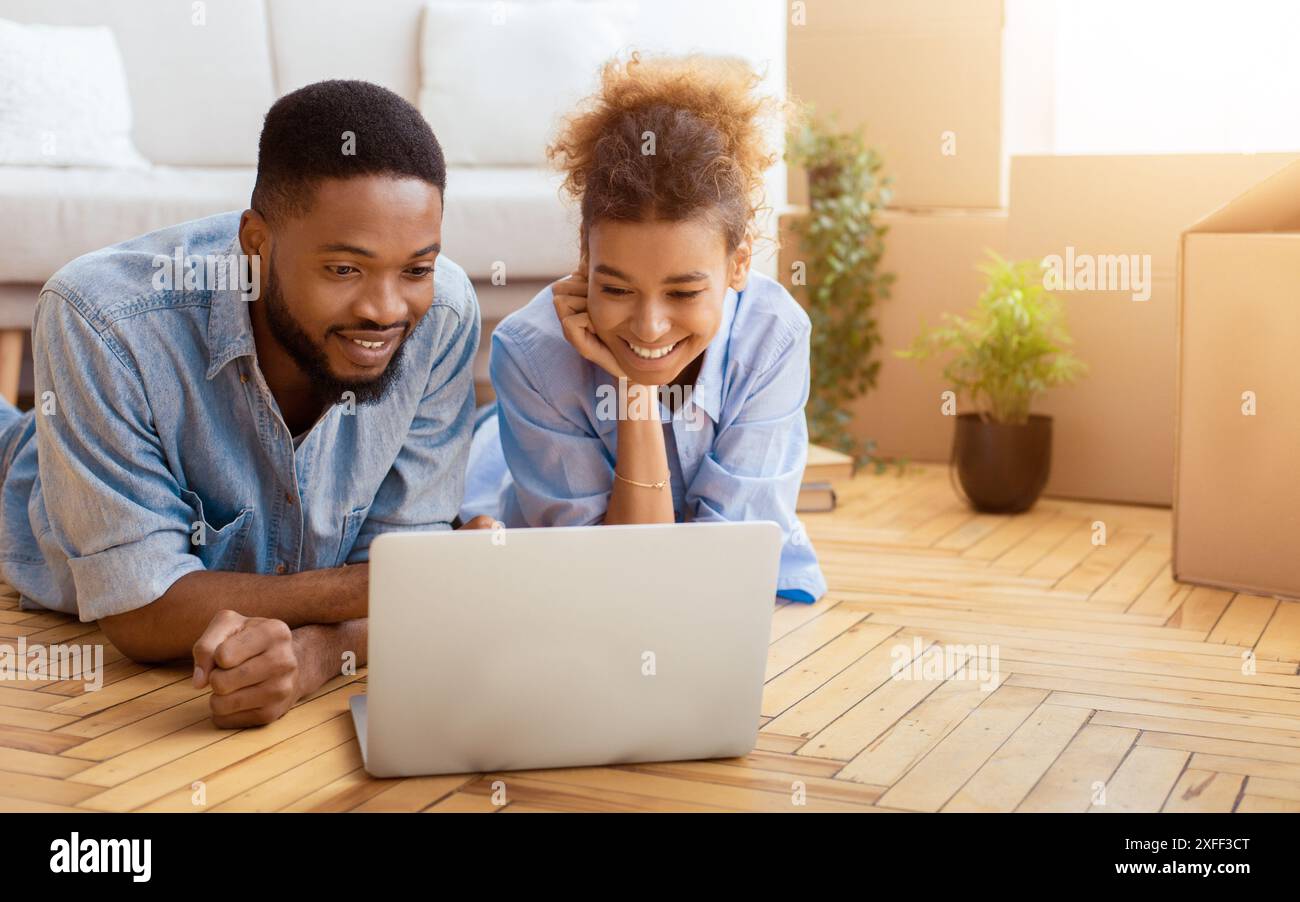 Black Spouses Using Laptop Lying On Floor Indoor Stock Photo