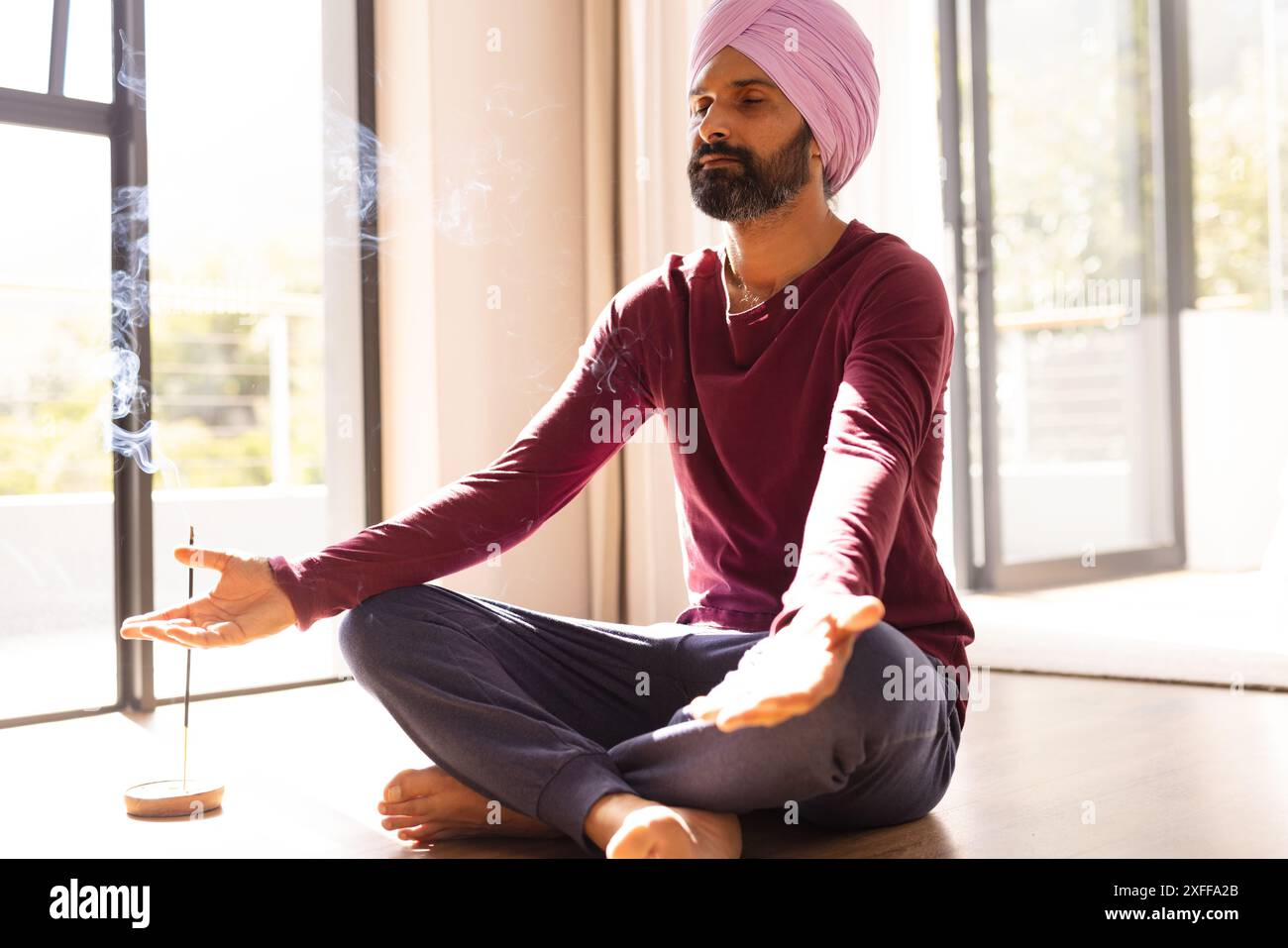 Meditating at home, Indian man sitting cross-legged with incense burning Stock Photo