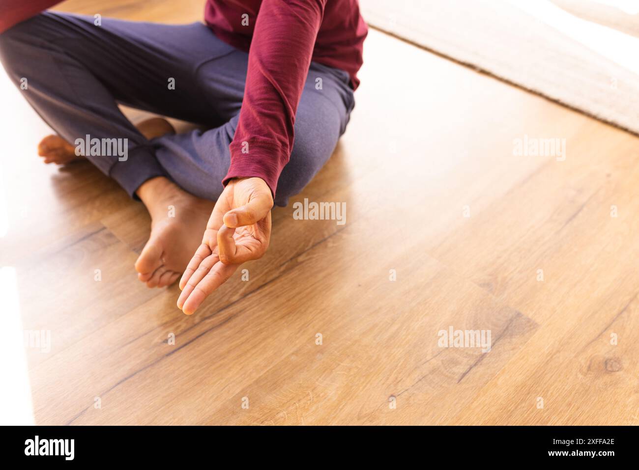 Practicing yoga, man sitting cross-legged on wooden floor, meditating at home Stock Photo