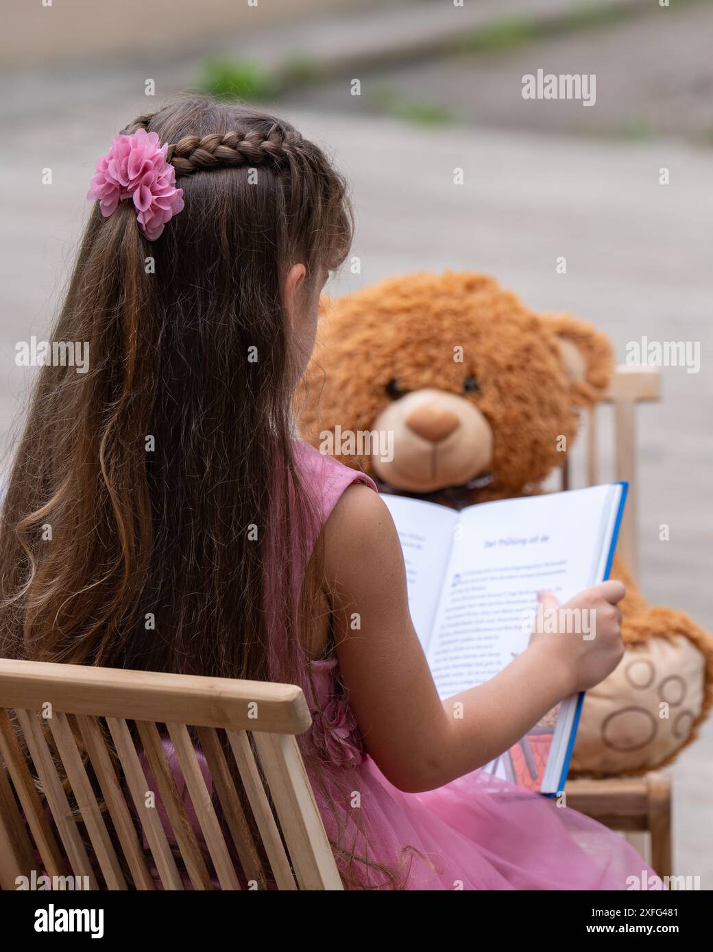 A small, cute girl with dark long hair sits on a chair and reads an ...