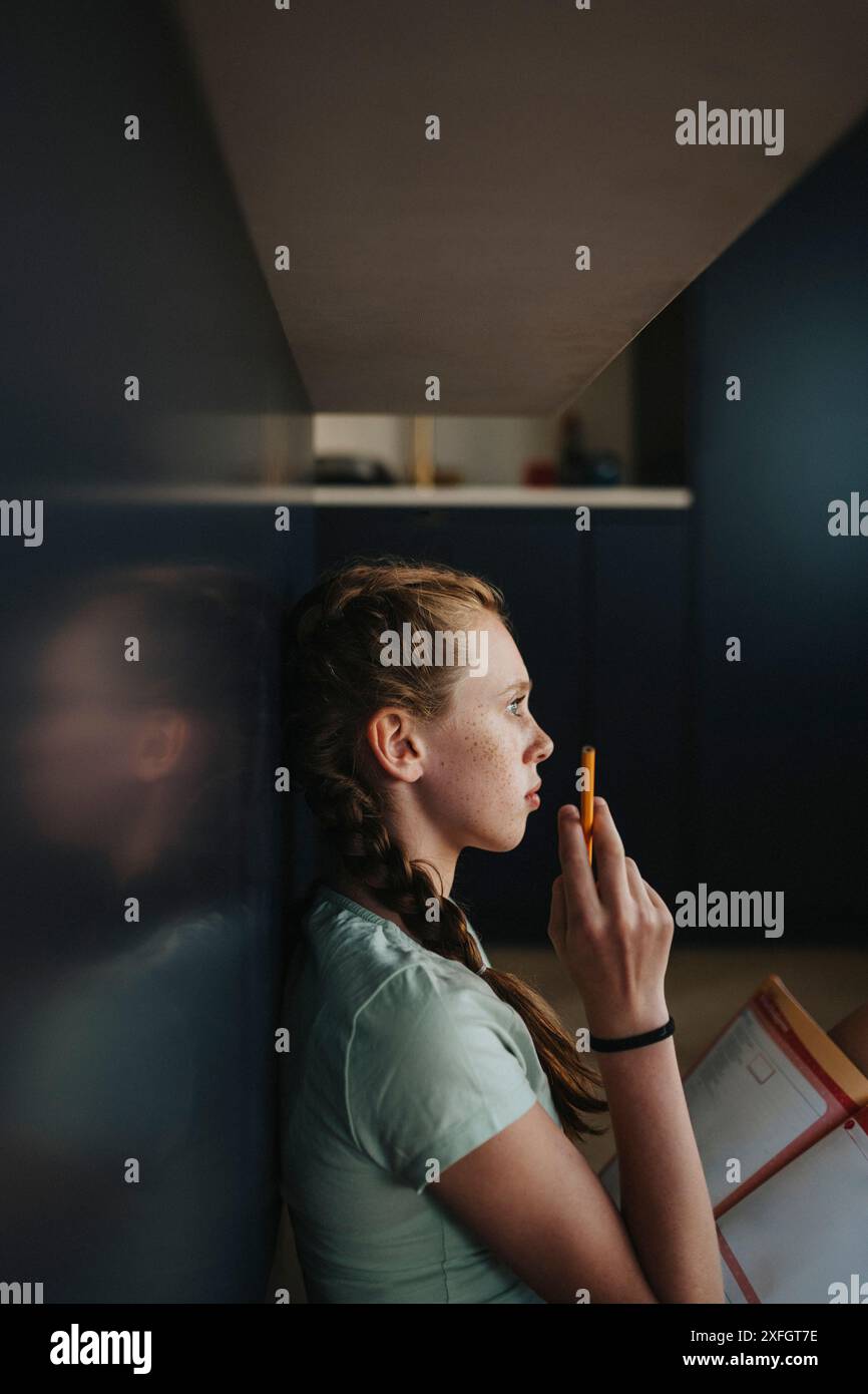 Thoughtful girl leaning on table while studying at home Stock Photo - Alamy