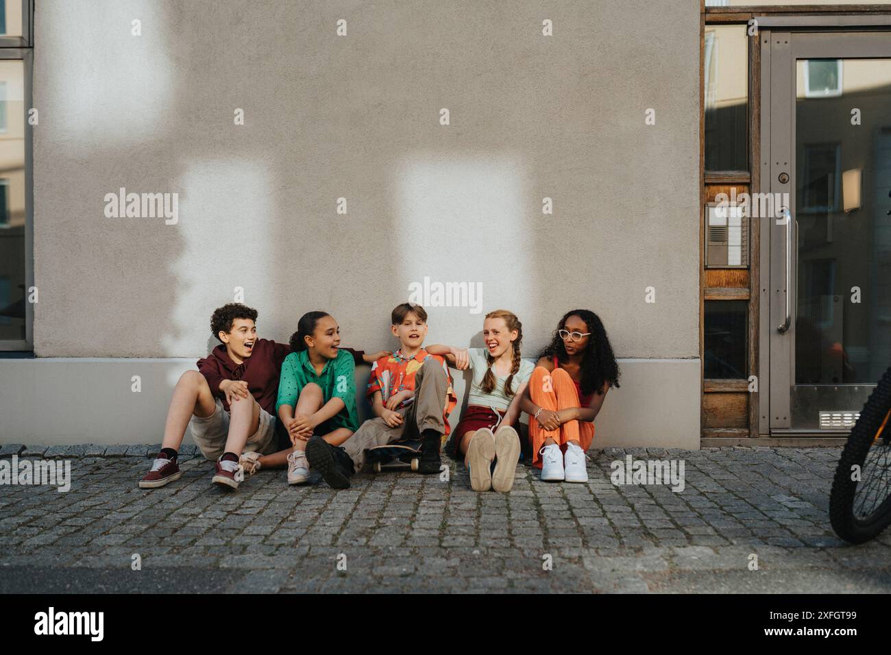 Happy boys and girls sitting on ground against wall Stock Photo