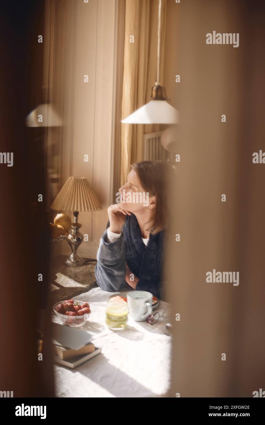 Senior woman sitting with hand on chin near dining table at home Stock Photo