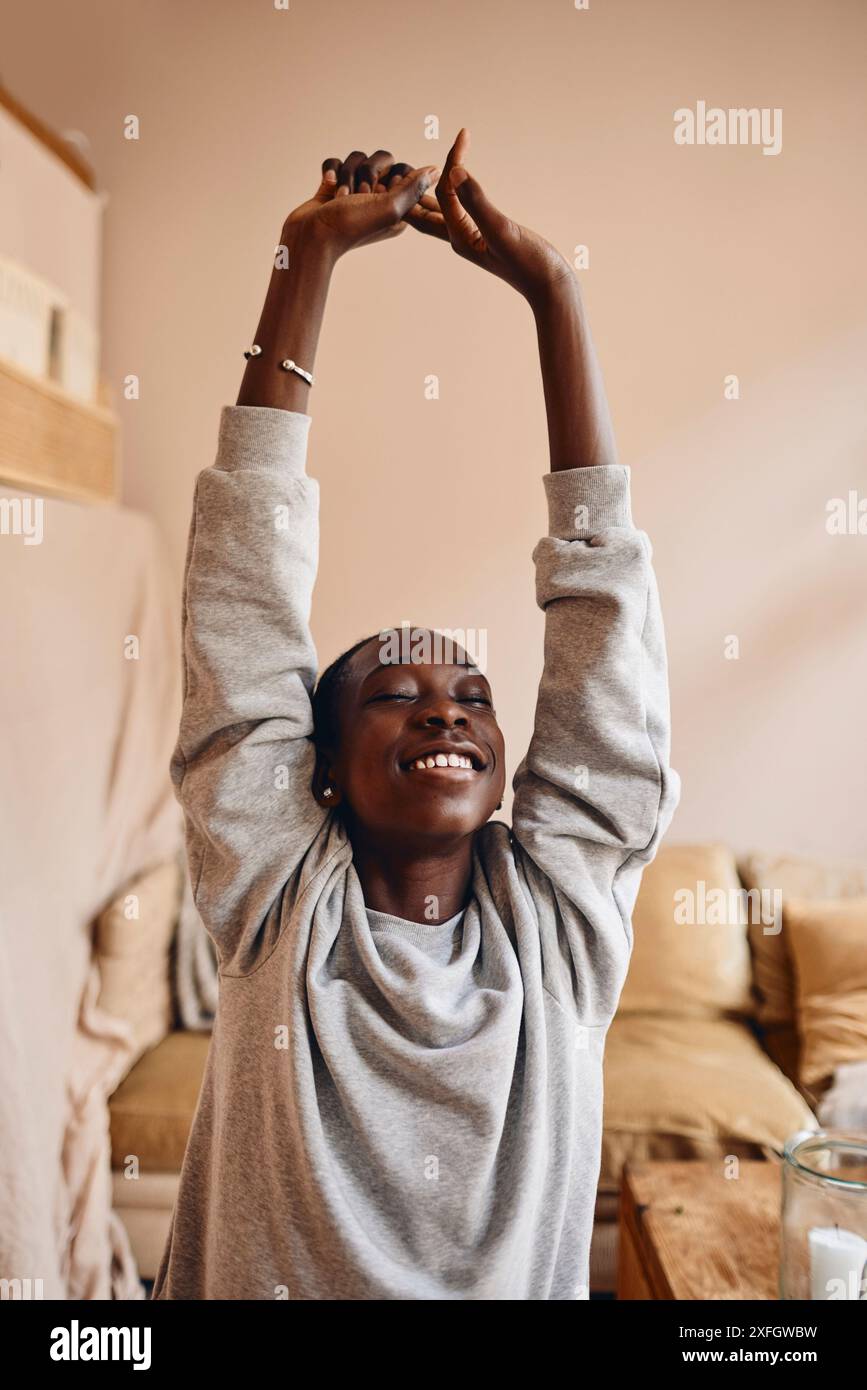 Smiling teenage boy stretching arms while doing yoga at home Stock Photo