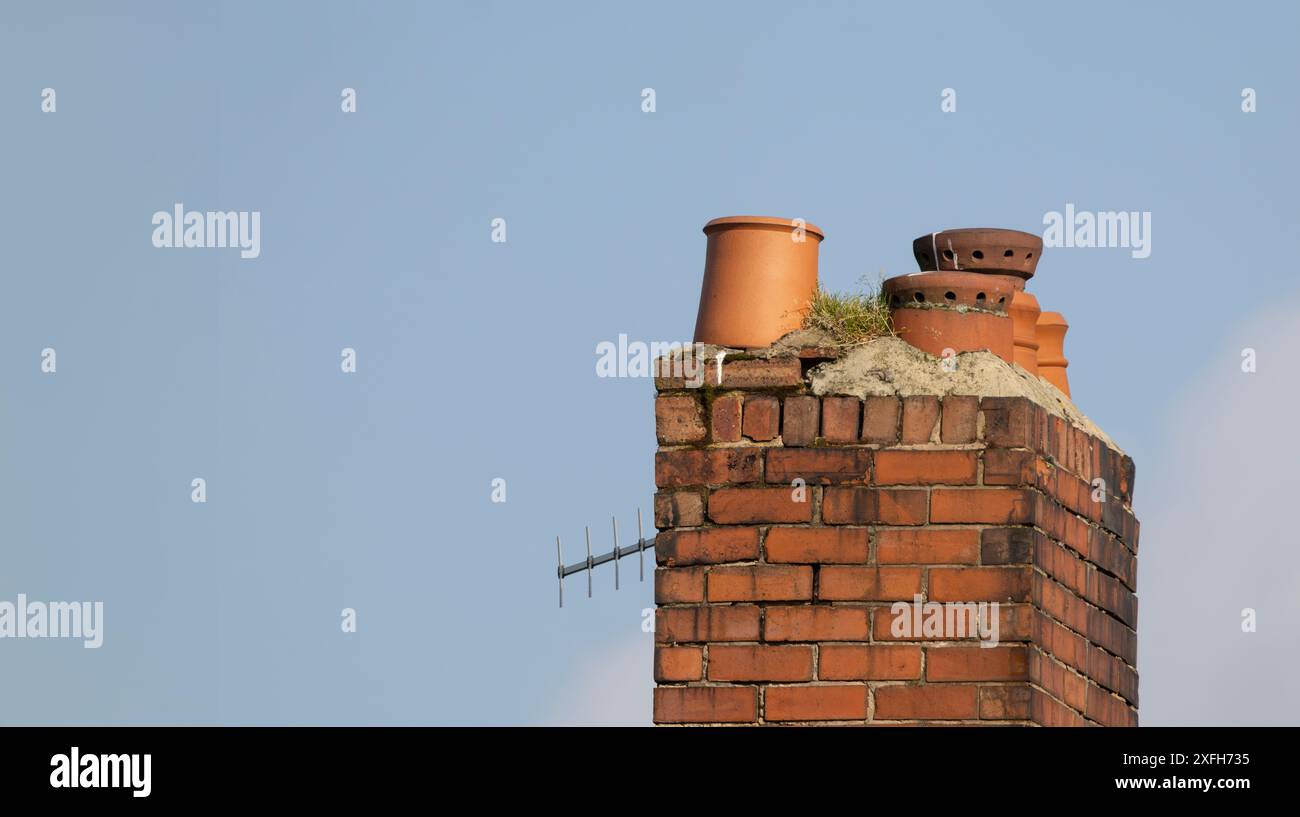 old weathered chimney stack with ceramic chimney pots against a clear blue sky Stock Photo