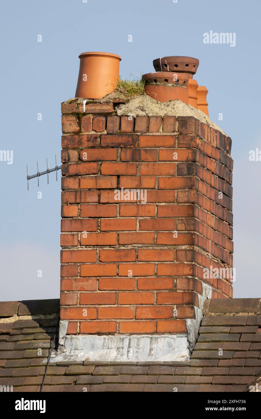 old weathered chimney stack with ceramic chimney pots against a clear blue sky Stock Photo