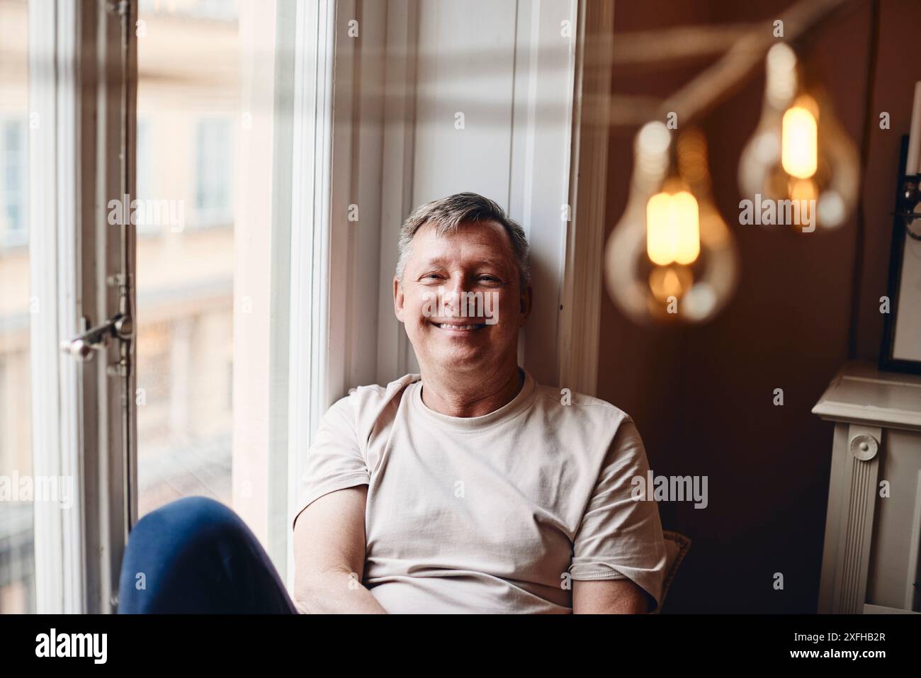 Portrait of smiling mature man sitting near window at home Stock Photo