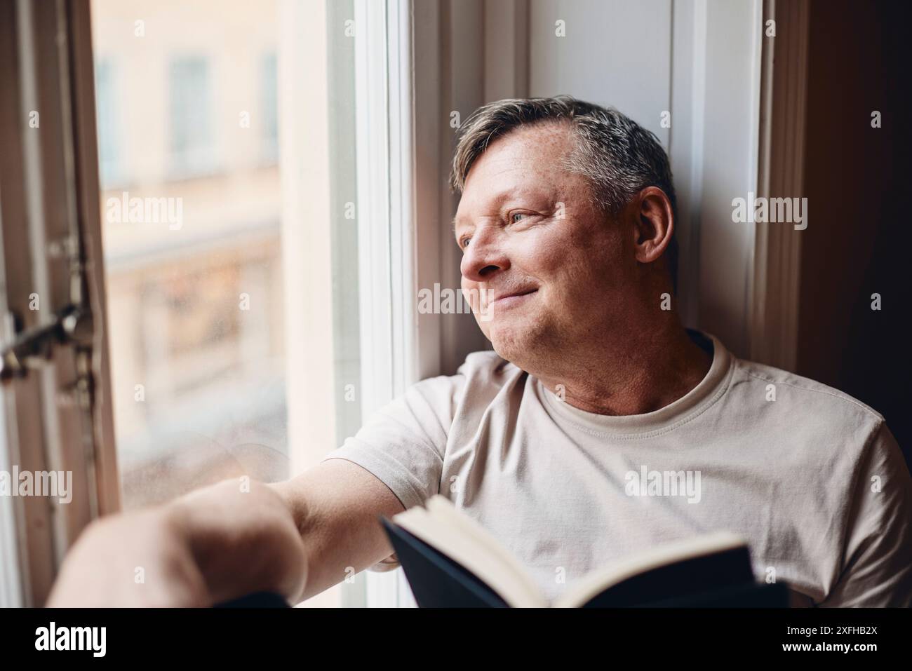 Thoughtful mature man looking through window at home Stock Photo