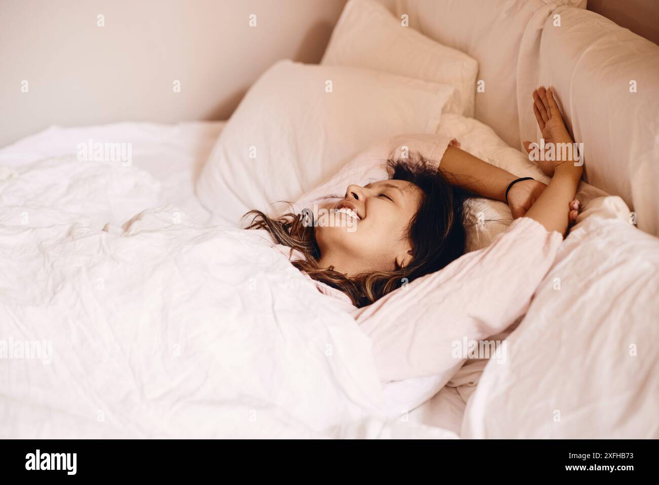 Smiling young woman lying down on bed at home Stock Photo