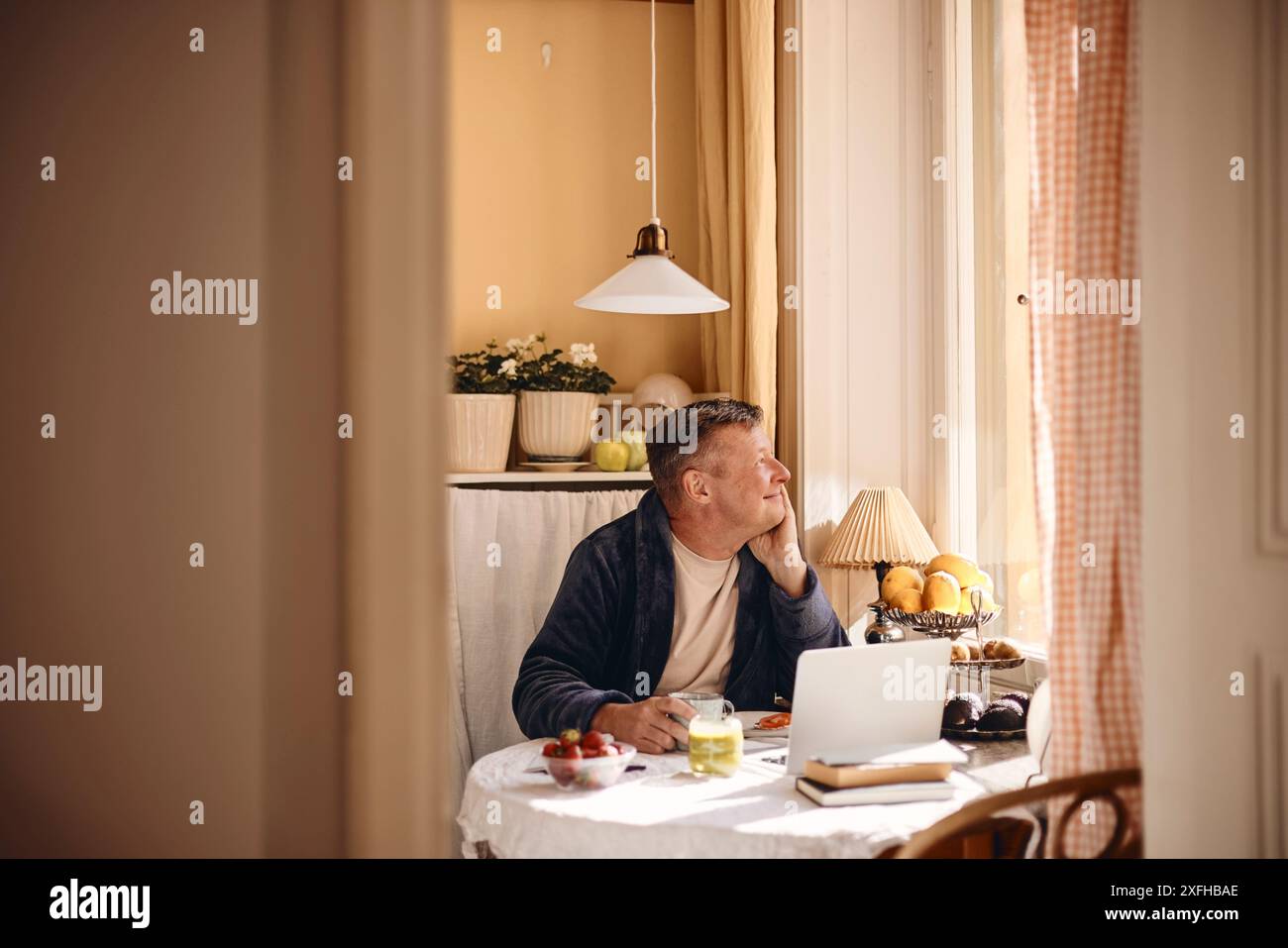 Thoughtful mature man looking through window while sitting at dining table Stock Photo