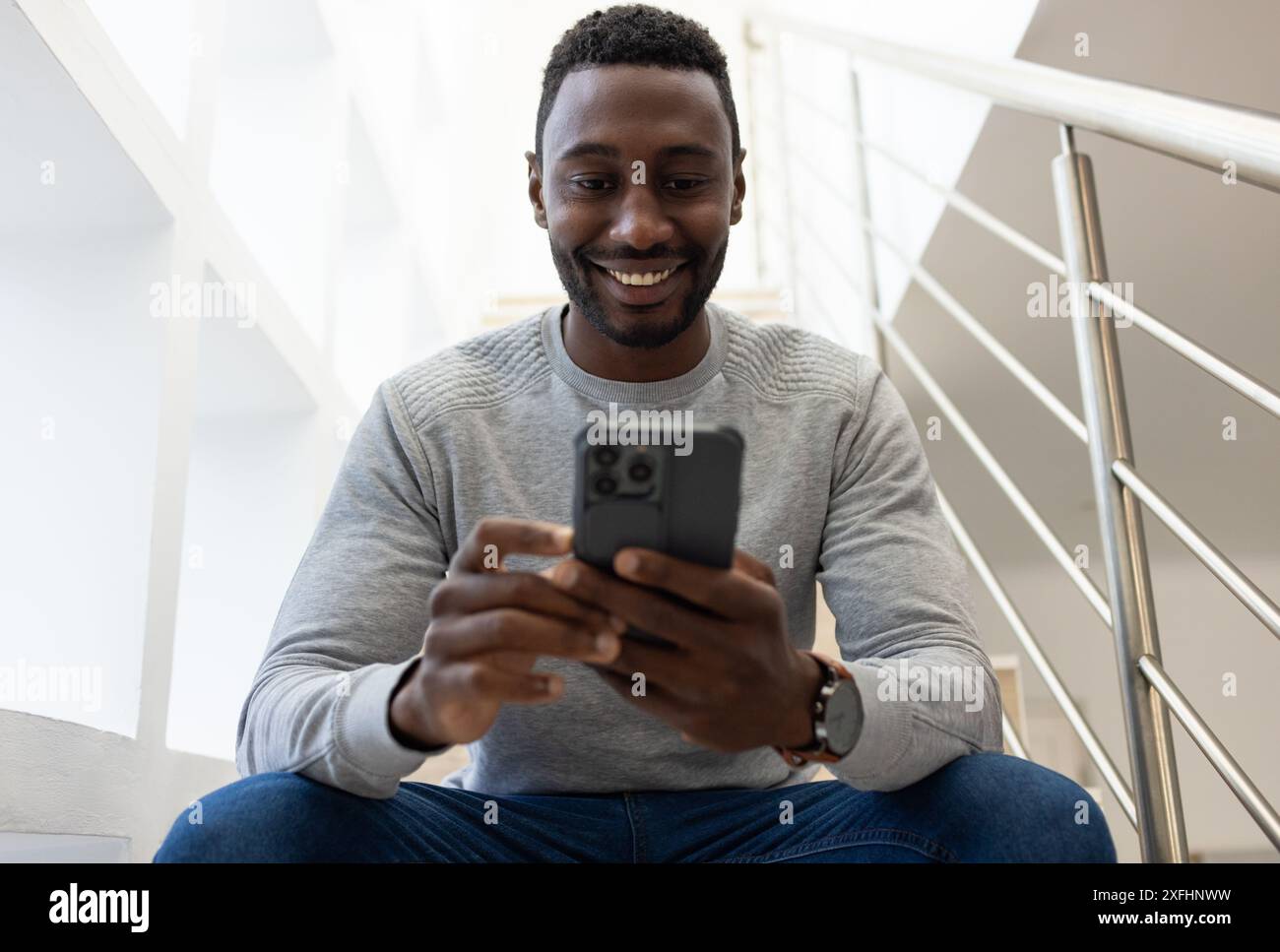 Smiling man using smartphone while sitting on stairs at home Stock Photo