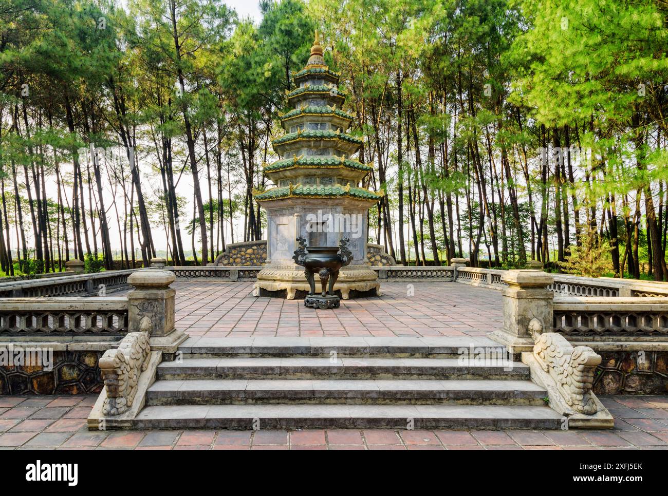 Scenic tower and black urn for burning incense among green trees at the Pagoda of the Celestial Lady (Thien Mu Pagoda) in Hue, Vietnam. Stock Photo