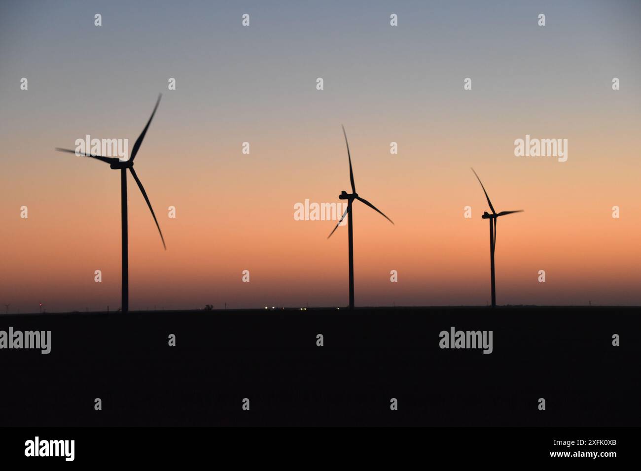 Silhouette of wind turbines against a colorful sunset sky in a rural ...