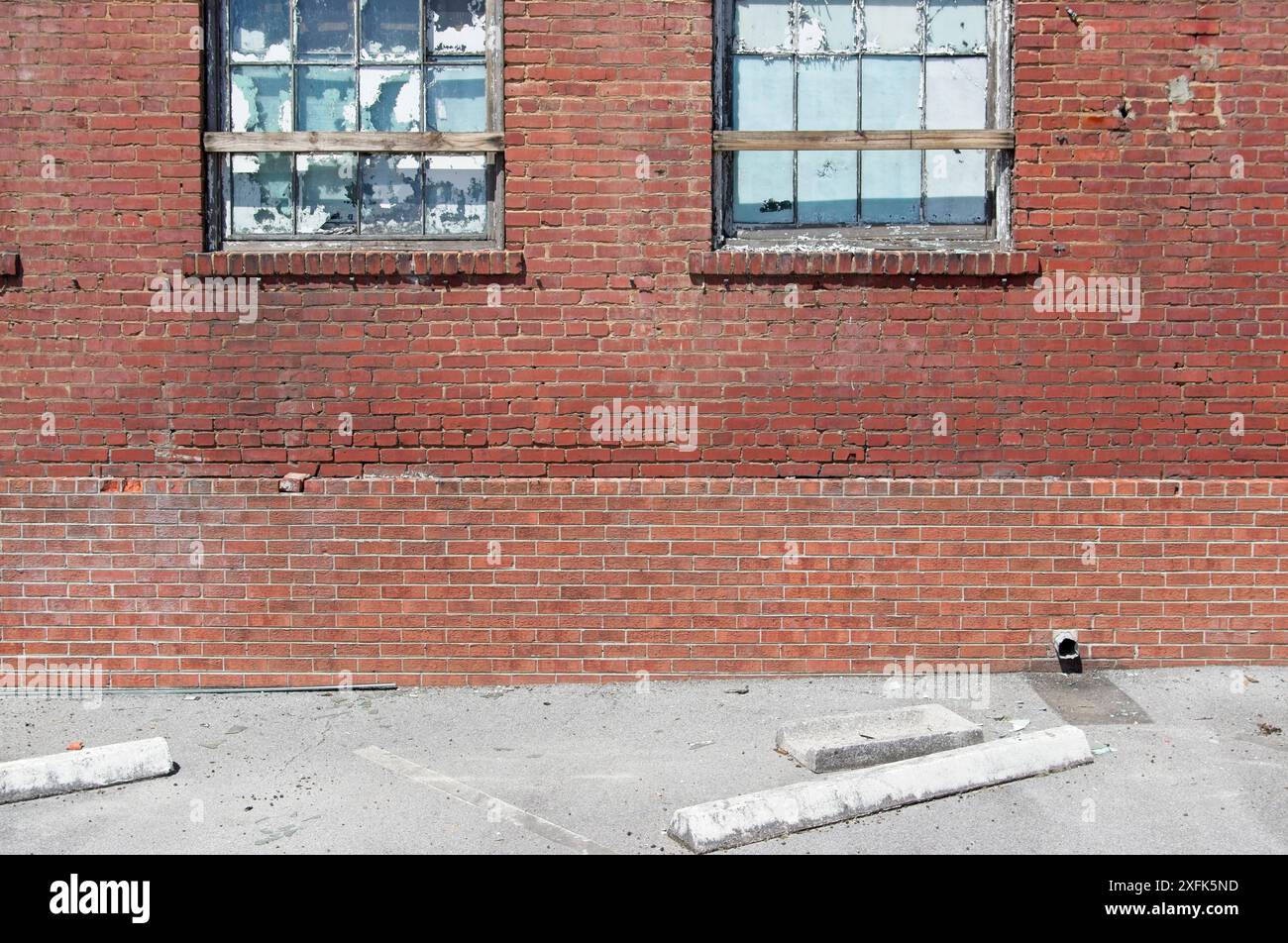 Abandoned brick industrial building with broken and weather worn windows next to parking bumpers Stock Photo