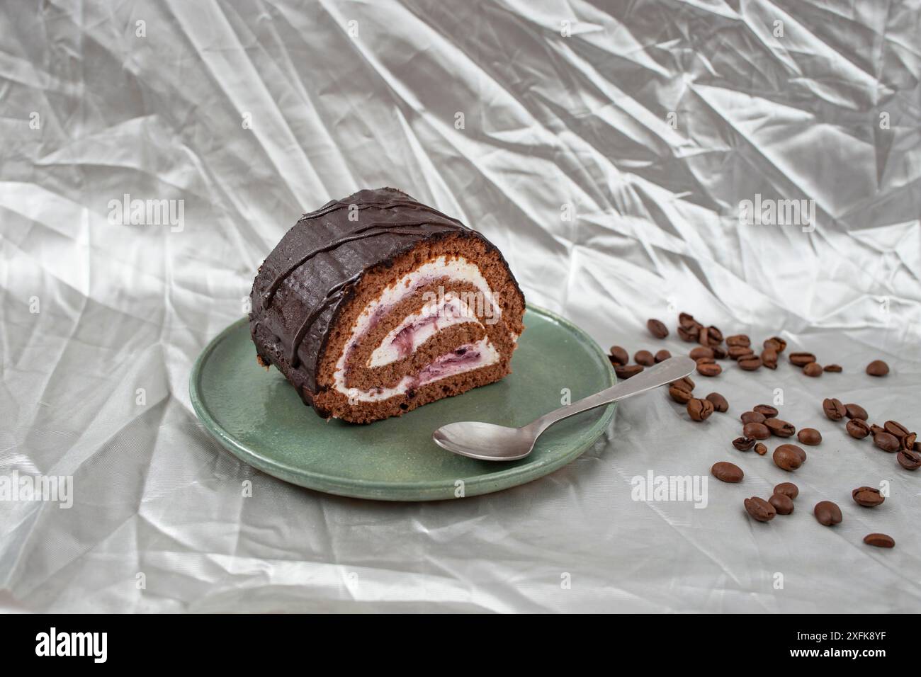 Chocolate roll with cheese and forest fruits filling and coffee beans on a ceramic plate, on silver Stock Photo