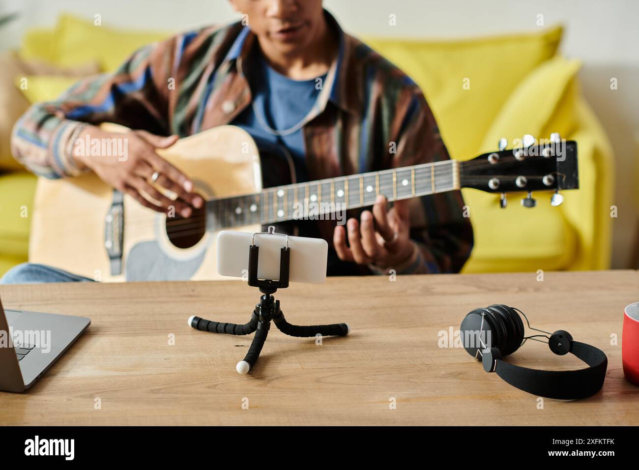 A young African American musician plays an acoustic guitar on a table while filming for his blog. Stock Photo