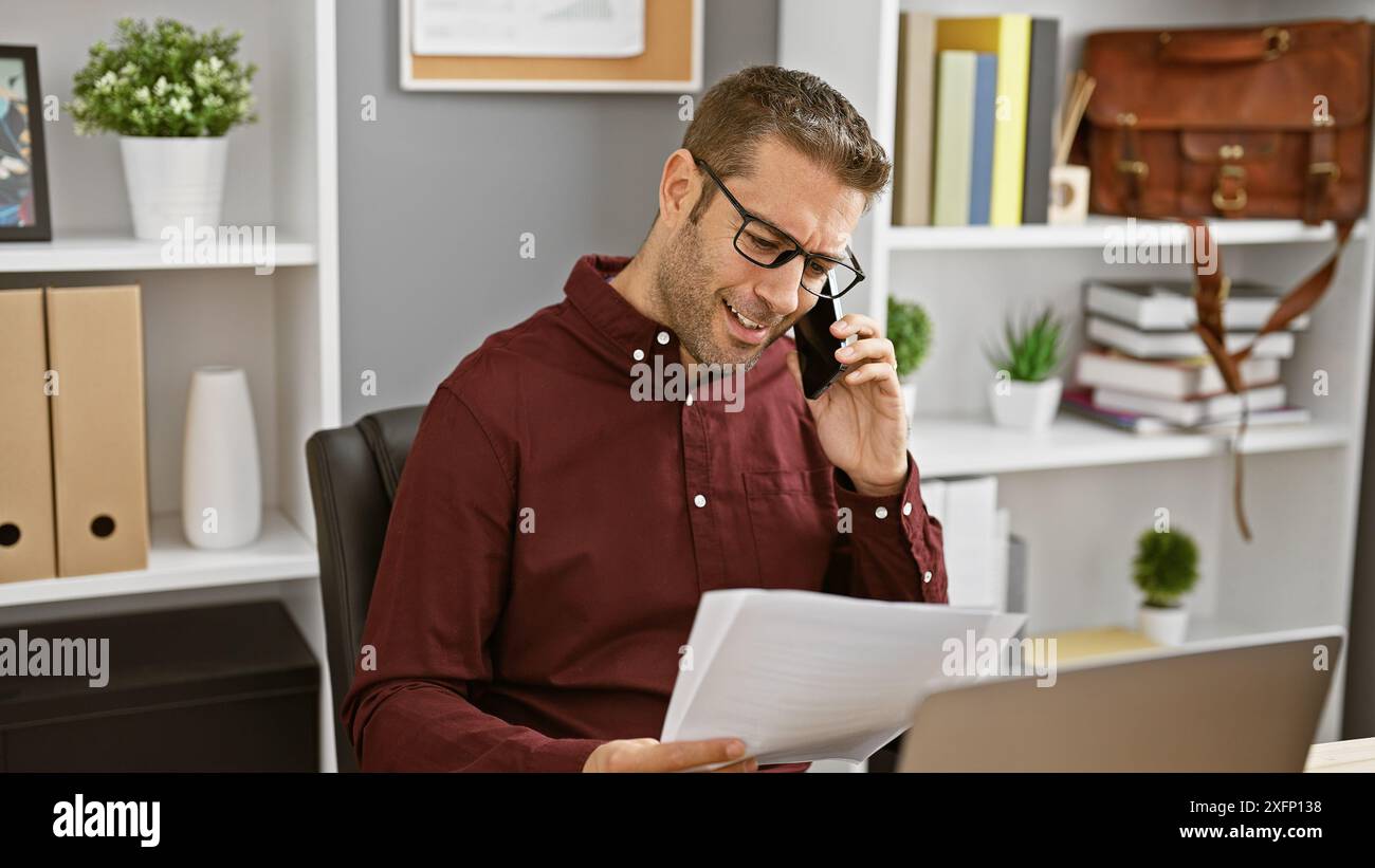 Smiling hispanic man in an office engaging in business over the phone while reviewing documents. Stock Photo
