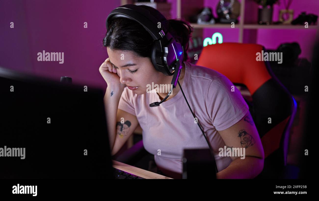 A thoughtful hispanic woman wearing headphones focuses on a computer in ...