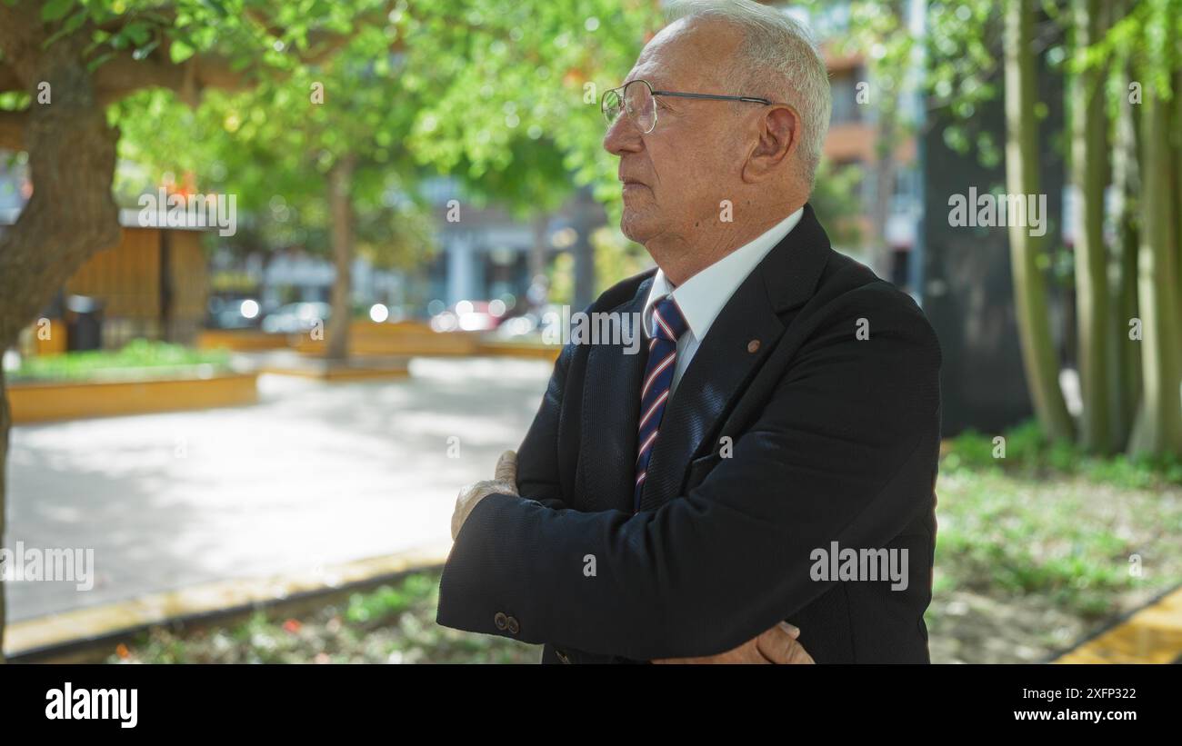 Elderly caucasian man in a suit and tie stands with crossed arms in an ...